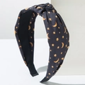 Detail of knotted black fabric headband with yellow star and moon print on plaster block - Black