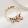 Detail eines goldenen Netzarmbands mit rosa Kristallherz, Emailleblume und Glasperle - Rosa