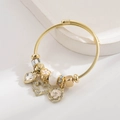 Detailaufnahme des goldenen gedrehten Armreifs mit Herzanhängern und Blumenperlen - Weiß