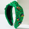 Detail eines grünen Knoten-Haarbandes mit Mardi-Gras-Silikonfiguren und glänzenden Steinen - Grün