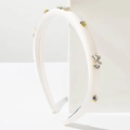 Detailed view of white satin headband with colorful rhinestones on a white pedestal - White
