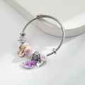 Dettaglio del bracciale in acciaio con pony viola, charm Gemini e ciondoli floreali - Viola