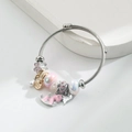 Dettaglio del bracciale a cavo argento con fiori in smalto rosa e ciondoli a cuore in luce soffusa - Rosa