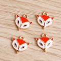 Nahaufnahme von vier Fuchs-Emaille-Anhängern mit goldenen Metallschlaufen auf Holz - Rot