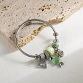 Detailed close-up of a silver charm bracelet with green faceted beads and heart pendant - Green