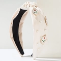 Close-up of a knot headband with pearls and a rose metal charm on a white fabric - Beige