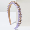 Detailed view of lavender satin padded headband with purple rhinestones on a white stand - Purple