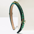 Close-up of velvet headband with emerald crystals and gold bee jewelry on white stand - Green
