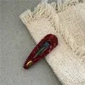 Close-up of a handmade red knitted drop hair clip with a golden metal tag detail - Teardrop Knitted Snap Clip (300-B263) / Burgundy
