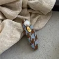 Dettaglio del fermaglio pied de poule con perla finta e targhetta in metallo dorato - Pied de Poule Ovale BB Clip / Blu Caffè