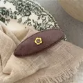 Macro detail of brown oval velvet hair clip with golden flower and purple gemstone inlay - Heather Grey