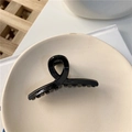Dettaglio di una molletta per capelli a torsione nera lucida su un piatto di ceramica - Nero