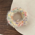 Close-up of a handmade fluffy beige scrunchie with colorful pom-pom knit details - AB White