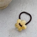 Gros plan d'un charme fleur en résine jaune à texture d'encre sur un élastique à cheveux - Beige
