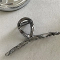Detailed macro view of gunmetal liquid metal hair claw with streamlined twist design - Shiny Gunmetal