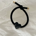 Close-up of black elastic hair tie featuring a glossy heart charm and gold metal caps - Black