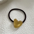Macro detail of elastic hair tie with a smooth amber-colored resin heart charm - Yellow