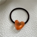Detailed close-up of amber orange heart charm on coffee brown high elastic hair tie - Orange