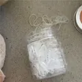 Detail view of transparent elastic hair bands in a clear jar with scattered rubber bands - 180 Pieces/Pack / Clear