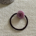 Detailaufnahme des rosa Harz-Rosen-Haargummis mit braunem Gummiband auf Weiß - Lila