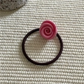 Detailaufnahme eines Haargummis mit rosa Harzrose und braunem Gummiband auf Stoff - Rosa