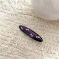 Detail of a glossy black oval hair clip with four pink bow patterns on a soft fabric - Black