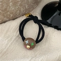 Vista macro di un elastico per capelli nero con perla smiley e piccolo ciondolo a cuore dorato - Marrone