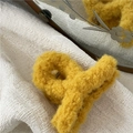 Close-up detail of a fuzzy yellow plush hair claw clip on a white textured background - Yellow