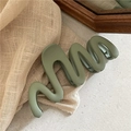 Détail d'une grande pince à cheveux mate verte au design ondulé sur un fond de tissu doux - Vert