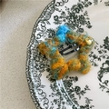 Dettaglio di un fermaglio per capelli a stella colorato in peluche con logo dorato su piatto - Etichetta Dorata Stella / Giallo Blu