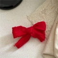 Detailed view of red knitted bow hair clip with warm wool texture on white fabric - Red