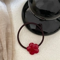 Close-up of a red acetate flower hair tie with a gold logo on a textured white fabric - Five-petal Flower Scrunchie / Burgundy