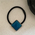 Detailed view of square peacock blue acetate hair tie with golden metallic trim and black band - Blue