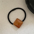 Close-up of orange acetate square charm with golden beads on black elastic hair tie - Tan