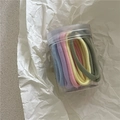 Gros plan d'élastiques à cheveux pastel assortis dans un pot de rangement transparent - Couleurs Crème