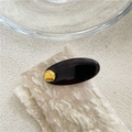 Makro-Aufnahme einer ovalen Acetat-Haarklammer mit goldenem Akzent auf beigem Untergrund - Punkt-Stil / Goldpunkt Schwarze Klammer