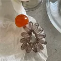 Dettaglio di elastico a spirale grigio con una grande perla arancione traslucida - Arancione