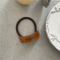 Detail of amber-toned tortoiseshell acetate hair tie on a minimalist grey stone surface - Brown