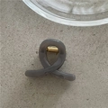 Detail view of a matte grey cross hair claw clip with golden metal spring on stone background - Gray