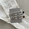 Vue détaillée de pinces à cheveux ondulées en métal argenté sur un carton gris texturé - Tête Ronde Ajourée