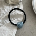 Detail shot of a black elastic hair tie featuring a pearlescent blue heart charm on paper - Blue Heart (Hair Tie)