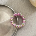 Close-up of pink telephone wire hair tie with colorful graffiti spots on a silver tray - Colorful Rose Purple