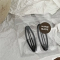 Detail of two black teardrop metal BB hair clips with handmade label in clear packaging - Small Black Oval Style