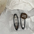 Detail view of two black oval BB hair clips with HAND MADE sticker in a poly bag - Large Black Oval Style