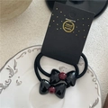 Dettaglio di elastici per capelli con fiocco nero e perle rosse su piatto ceramico - Elastico per capelli / Nero