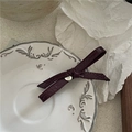 Dettaglio del fermaglio a fiocco in pelle bordeaux con logo dorato su piatto vintage - Rosso Vino (Placca Oro)