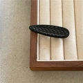 Detailaufnahme einer schwarzen Haarspange mit Webmuster auf elegantem Samttablett - Schwarzer Wassertropfen
