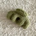 Detalle de la pinza de pelo de felpa verde oliva sobre fondo beige con textura cálida - Verde