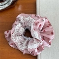 Detail eines rosa Blumen-Scrunchie mit weißem Spitzenbesatz auf einem Holztisch - Spitzenstil / Rosa Große Rose Spitze