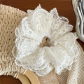 Détail d'un chouchou en dentelle blanche avec broderie florale sur un sac en paille - Blanc Cassé